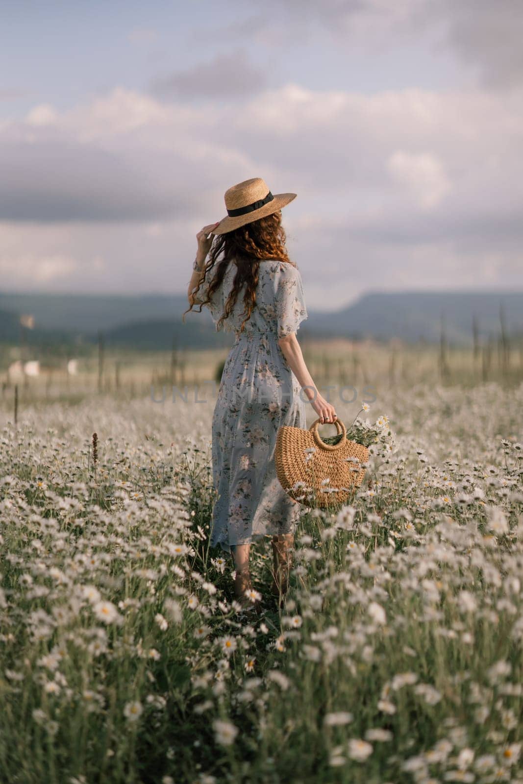 A woman is walking through a field of flowers, wearing a straw hat and carrying a basket. The scene is peaceful and serene, with the woman standing out against the backdrop of the colorful flowers. by Matiunina