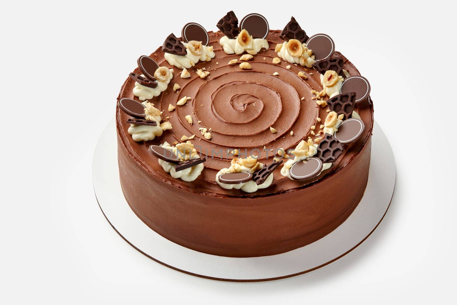 Elegant honey chocolate cake featuring smooth frosting topped with whipped cream swirls, chocolate honeycombs pieces and hazelnuts, presented on white stand