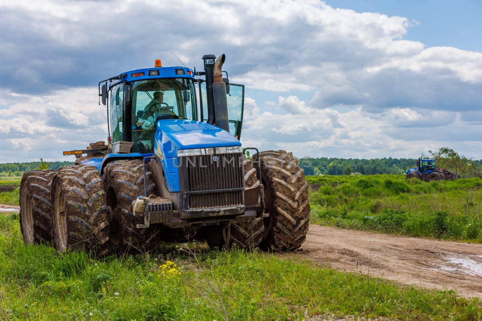 Blue New Holland tractor with double wheels standing near agricultural field at hot sunny day in Tula, Russia - June 4, 2022