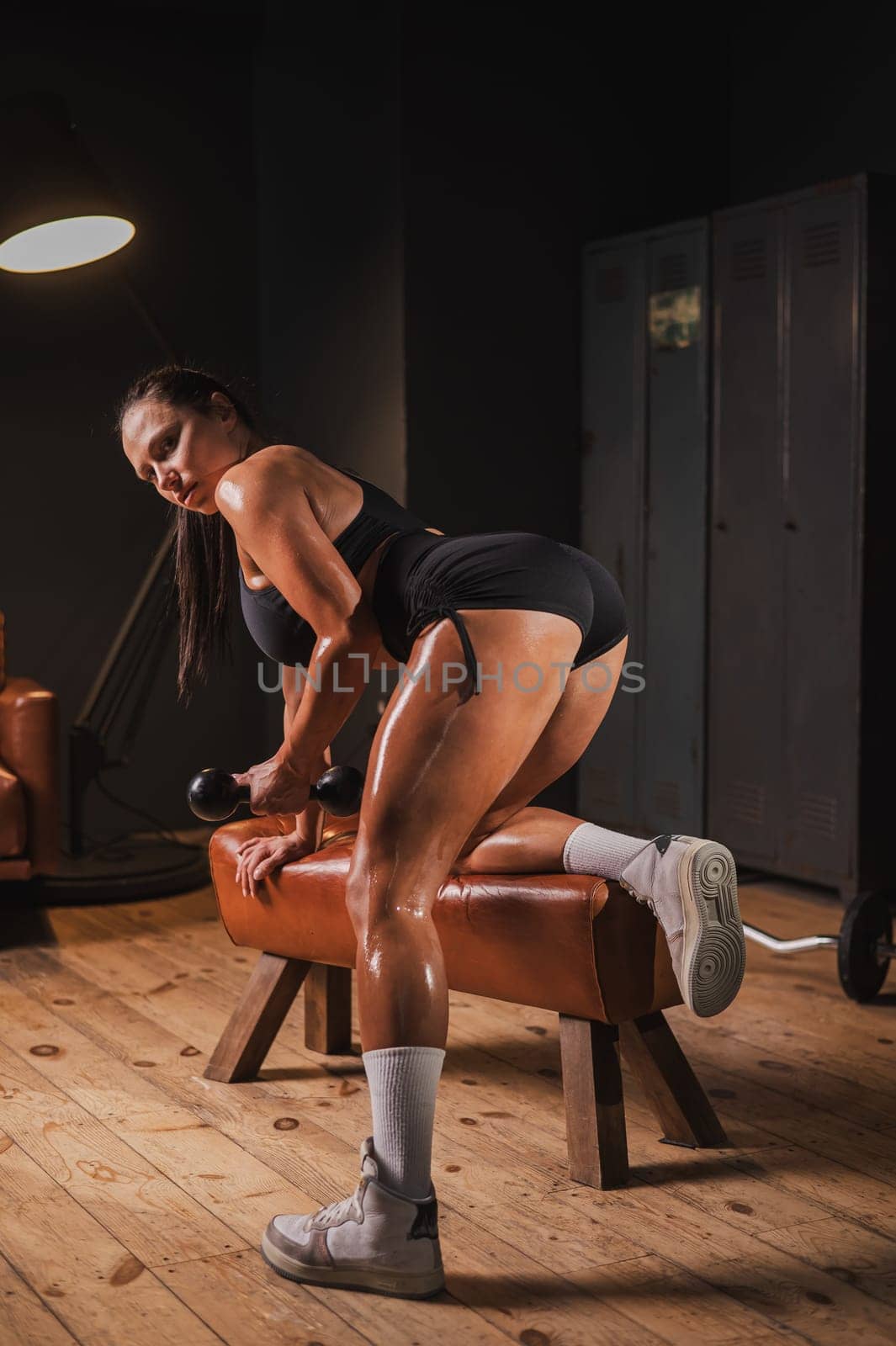Caucasian woman doing one arm dumbbell row on a bench in a retro gym. Vertical photo. by mrwed54