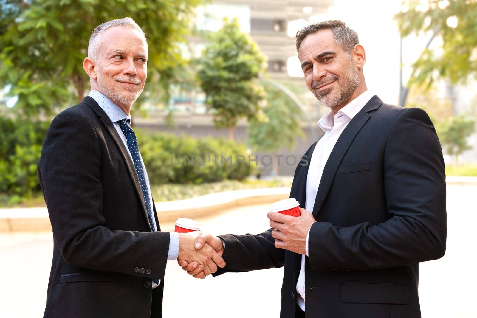 Two colleagues face each other, high-five, look at the camera, work as a team, ready to start a new project, pose outdoors