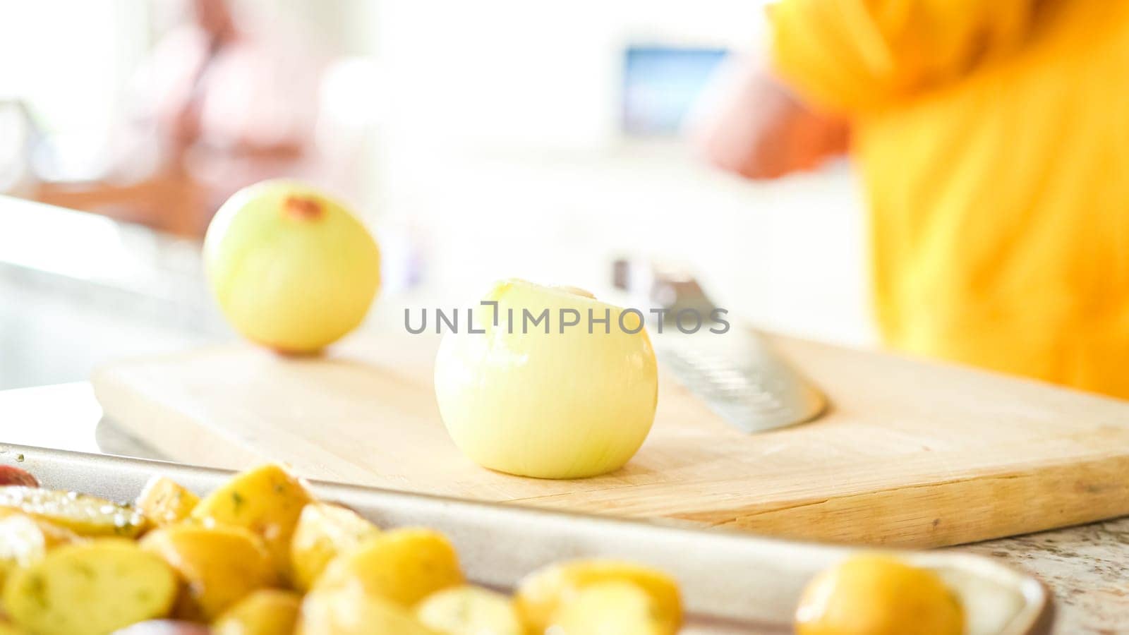 In the welcoming setting of a modern kitchen, a young man continues his dinner preparation process. He's currently involved in slicing yellow onions into rings, prepping them for grilling on an outdoor grill, a crucial step in creating a flavorful meal.