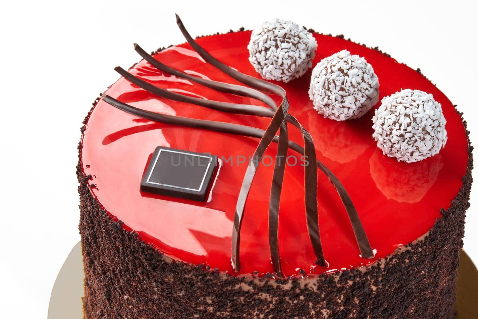 Stylish chocolate cake with glossy red glaze, adorned with dark chocolate curls and white coconut truffles. Handcrafted confectionery