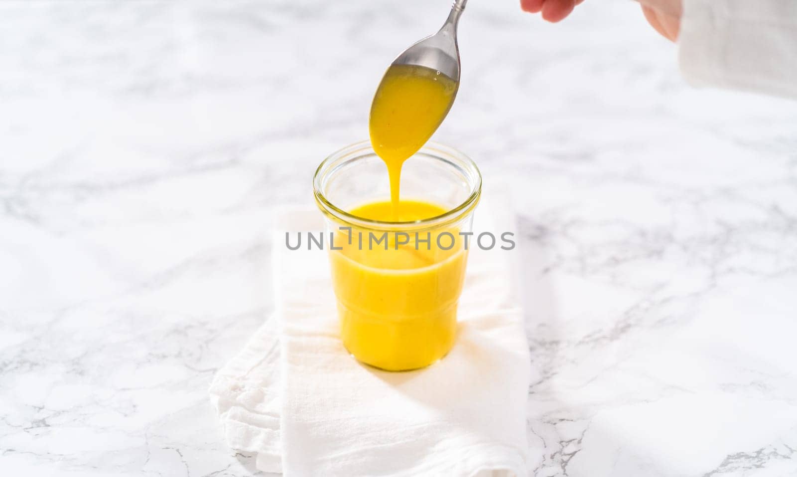 Homemade hollandaise sauce in a glass jar on a marble background.