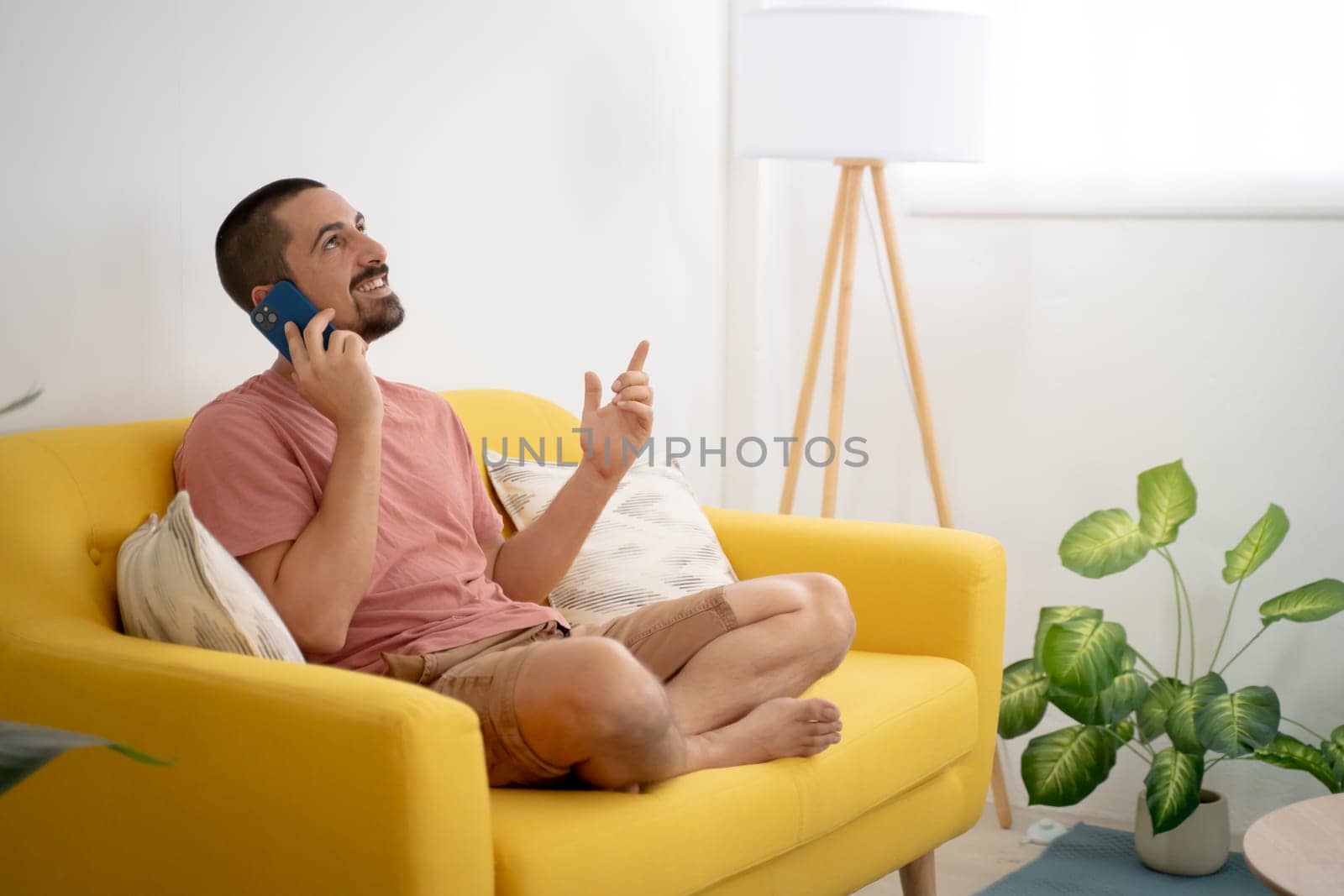 Smiling young man talking smartphone sitting on sofa at home. High quality photo