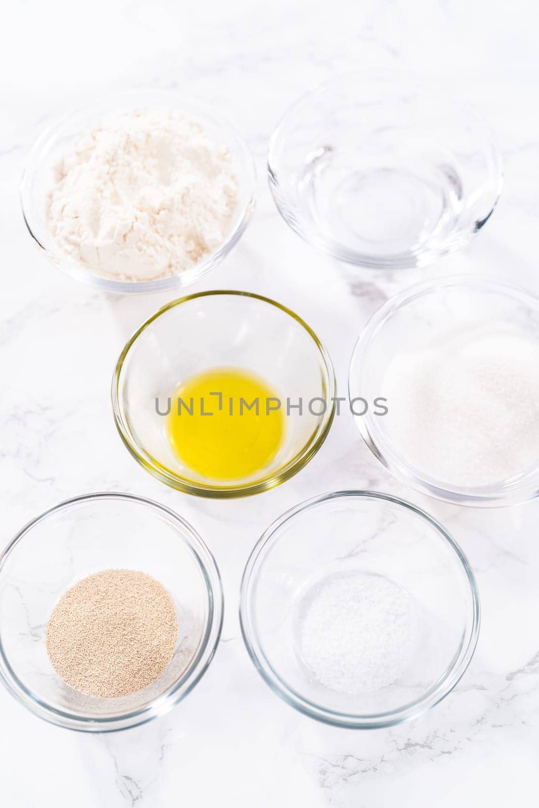 Measured ingredients in a glass mixing bowl to prepare pizza dough.