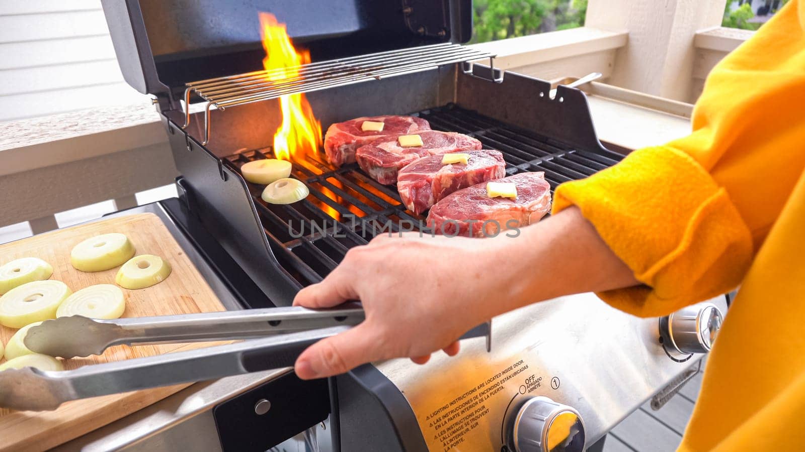 The outdoor two-burner gas grill is put to good use, sizzling with the sound and aroma of ribeye steaks and onion rings being perfectly cooked.