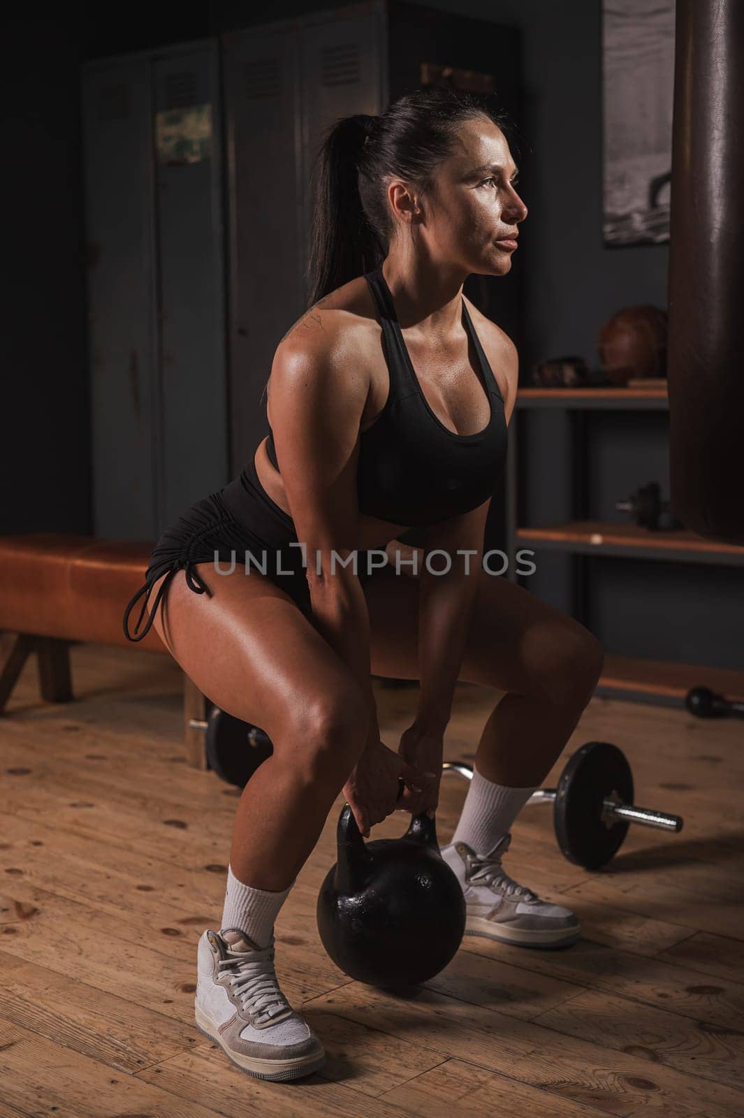 Caucasian woman doing squats with kettlebell in retro gym. Vertical photo