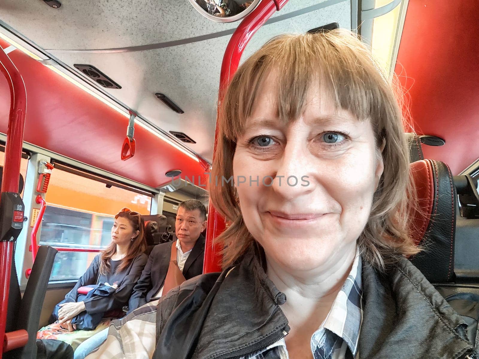 Hong Kong, China - April, 05, 2024: Smiling woman with fellow commuters on a red Hong Kong bus