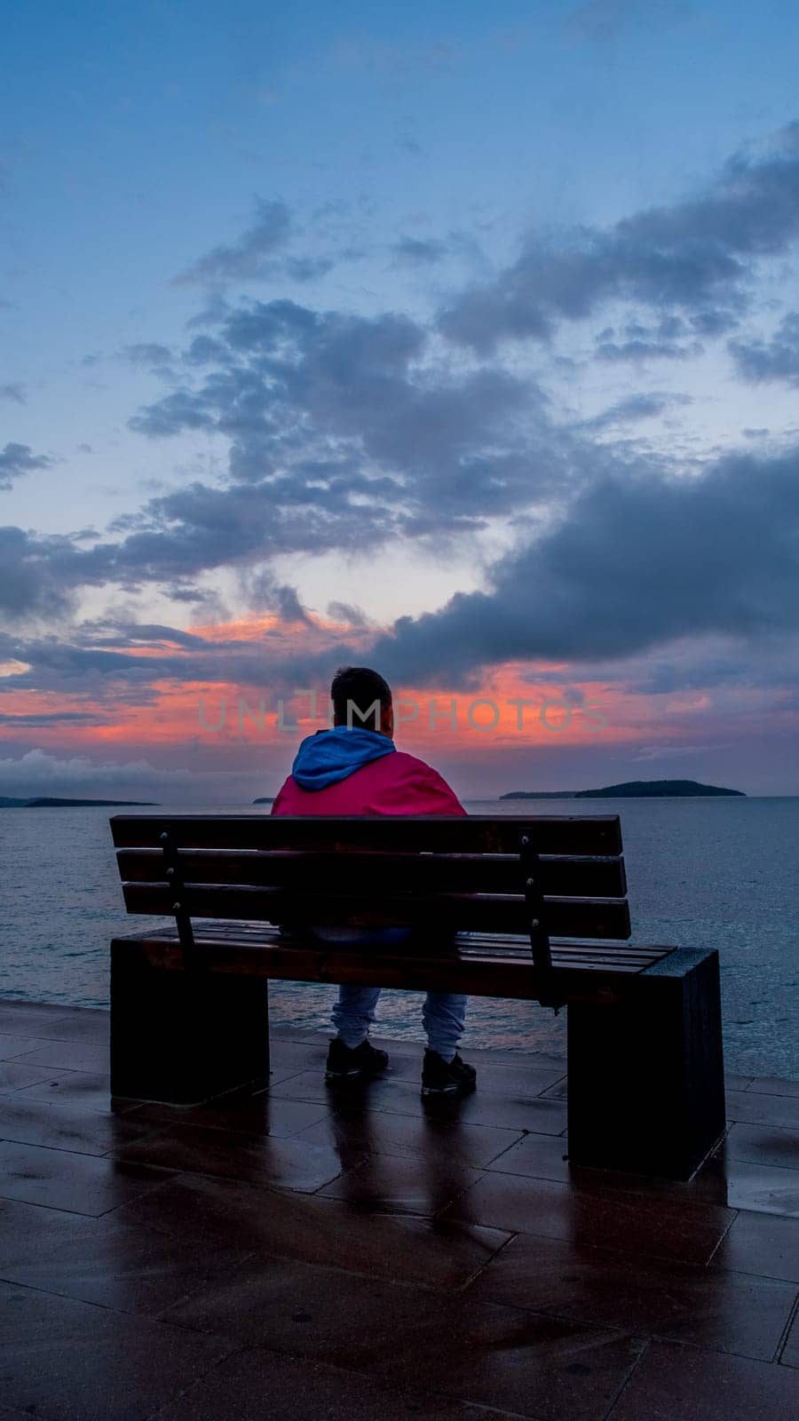 As the sun begins to set, a person sits on a bench by the ocean, watching the liquid gold reflections on the water while clouds paint the sky in hues of pink and orange