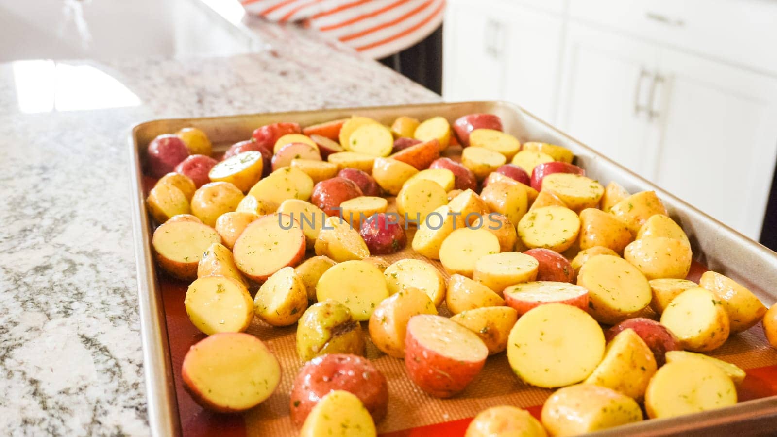 In a modern, white kitchen, a young man is engrossed in dinner preparations. His current endeavor includes arranging seasoned rainbow potatoes on a baking sheet, a meticulous step towards a promisingly tasty meal.