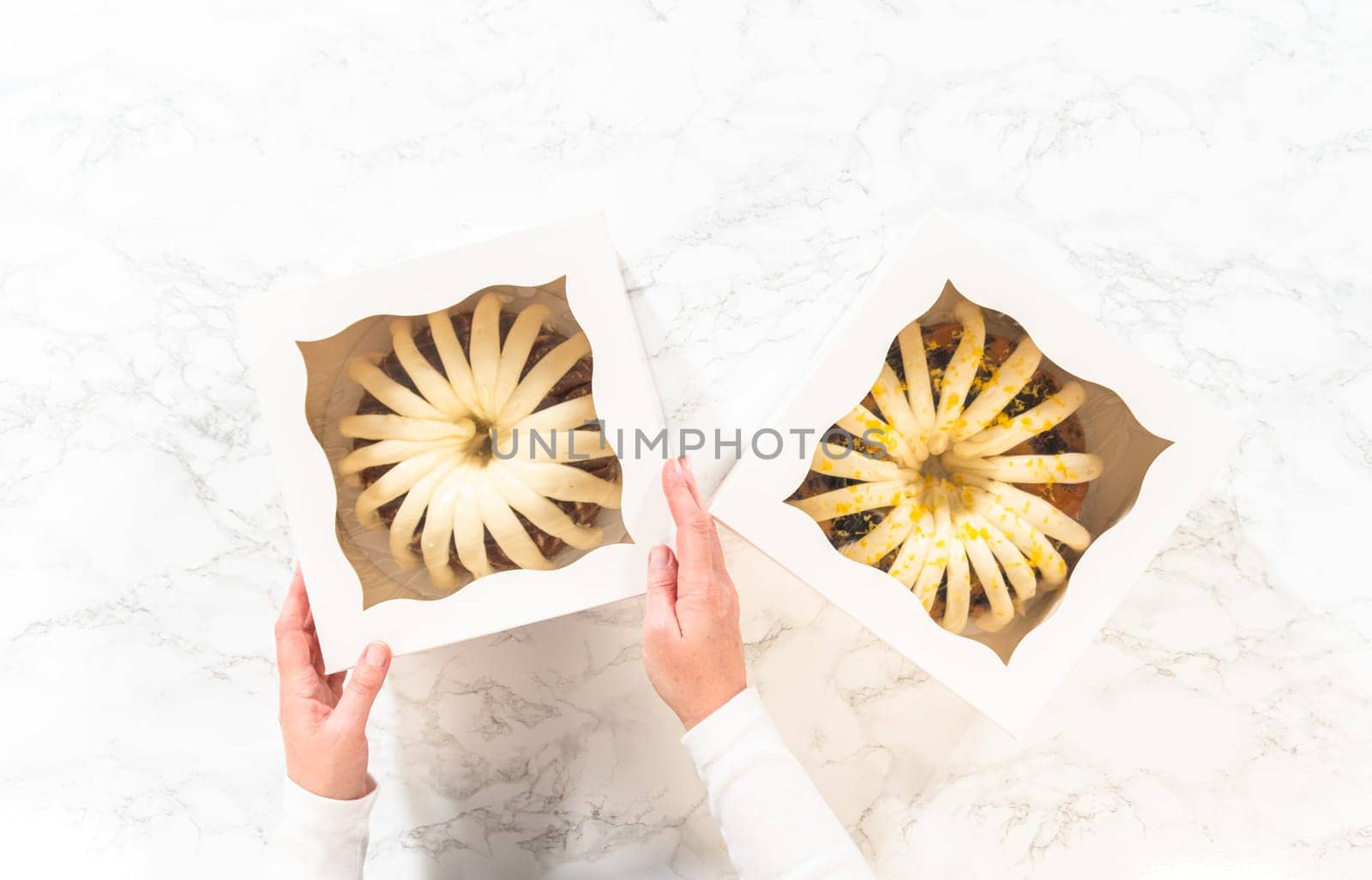 Flat lay. The freshly baked bundt cakes are carefully nestled into white paper boxes, preparing them for secure transportation while maintaining their delectable appearance.