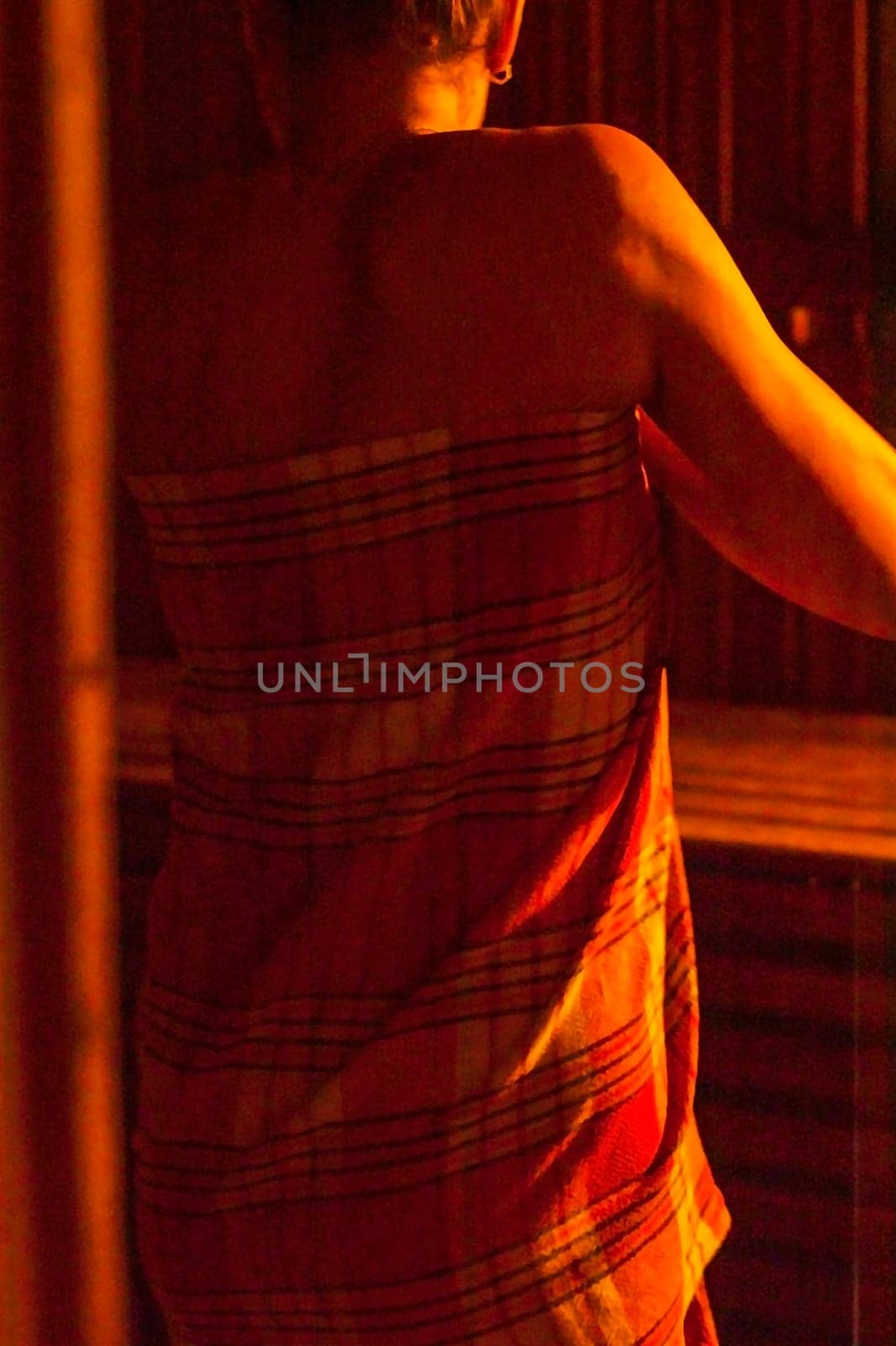 Shot of the woman with beautiful body, wrapped in checkered towel in the dark, warm sauna room