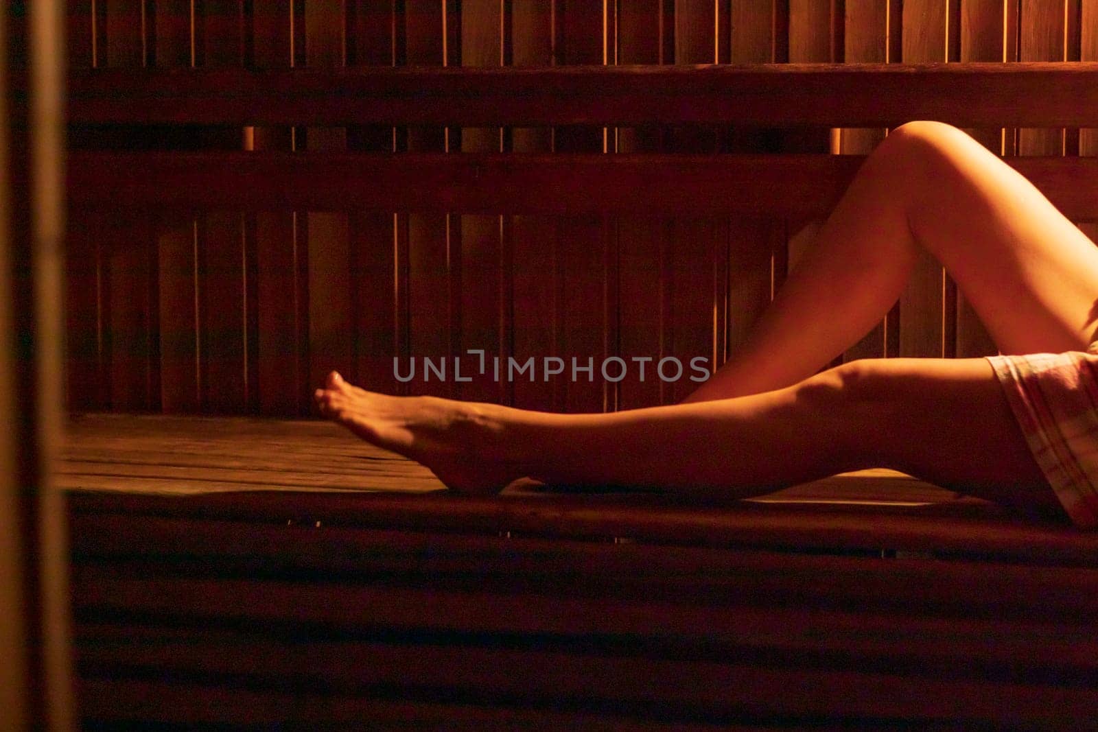 Shot of the woman with beautiful body, wrapped in checkered towel in the dark, warm sauna room