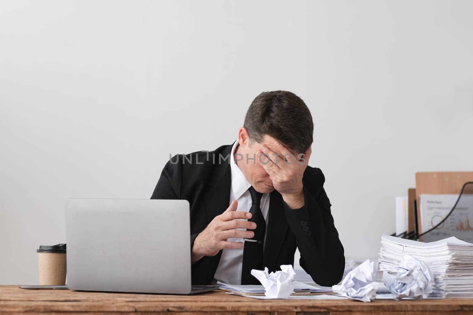 Businessman frustrated with crumpled papers at desk with laptop, concept of stress and problem-solving.