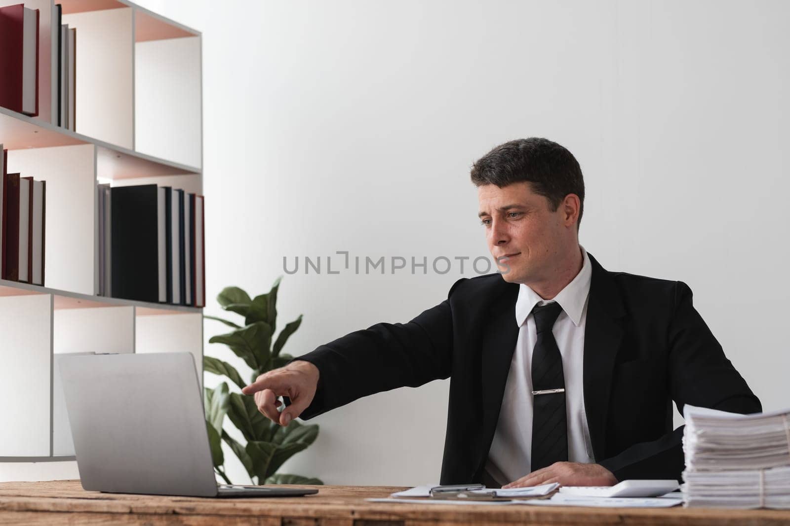 Businessman pointing at laptop screen in office, concept of focus and direction by wichayada