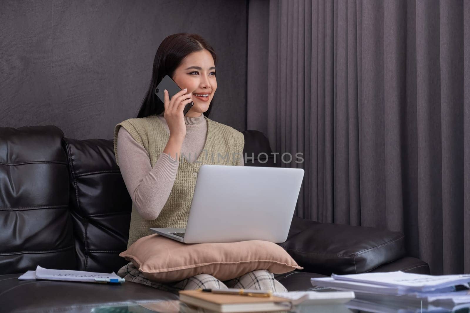 Woman Using Laptop and Smartphone on Sofa. Concept of multitasking and modern lifestyle..
