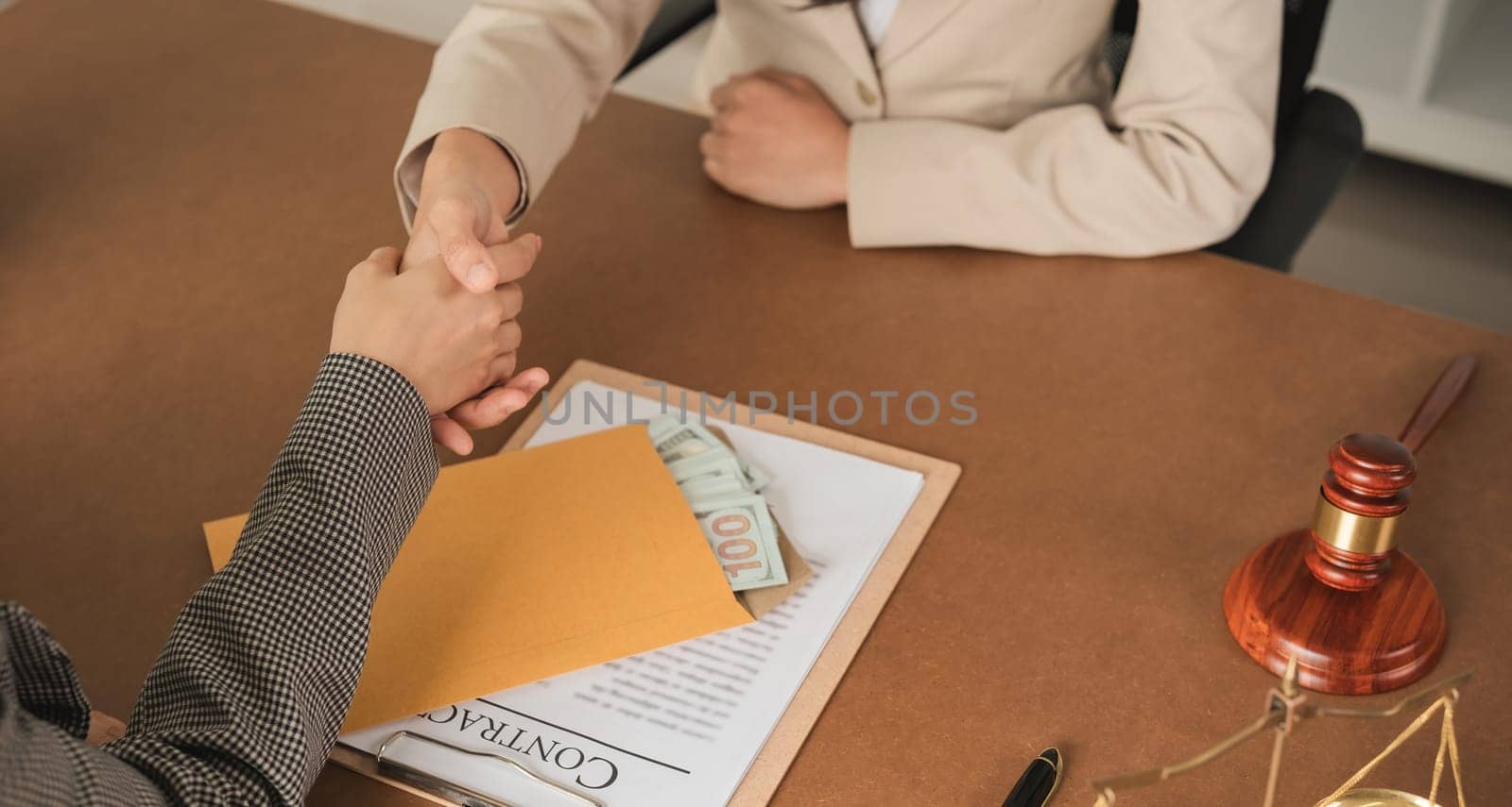 Close-up of business handshake with money in envelope on desk. Concept of business agreement and financial transaction.