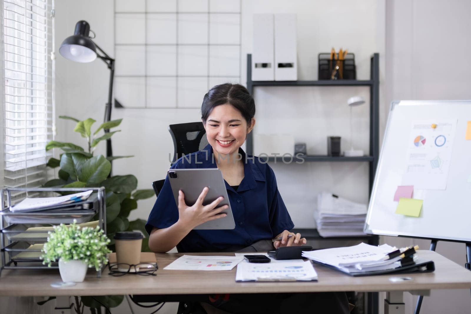 Young Asian woman using tablet in office workspace. Concept of business technology and productivity by wichayada