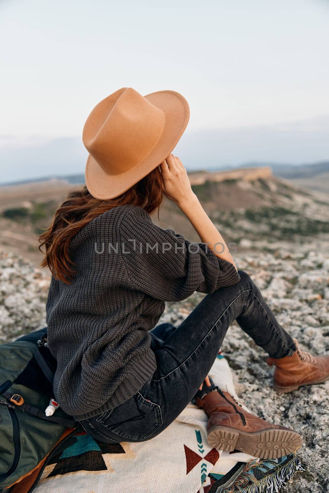 Woman in hat sitting on blanket with backpack, gazing at horizon
