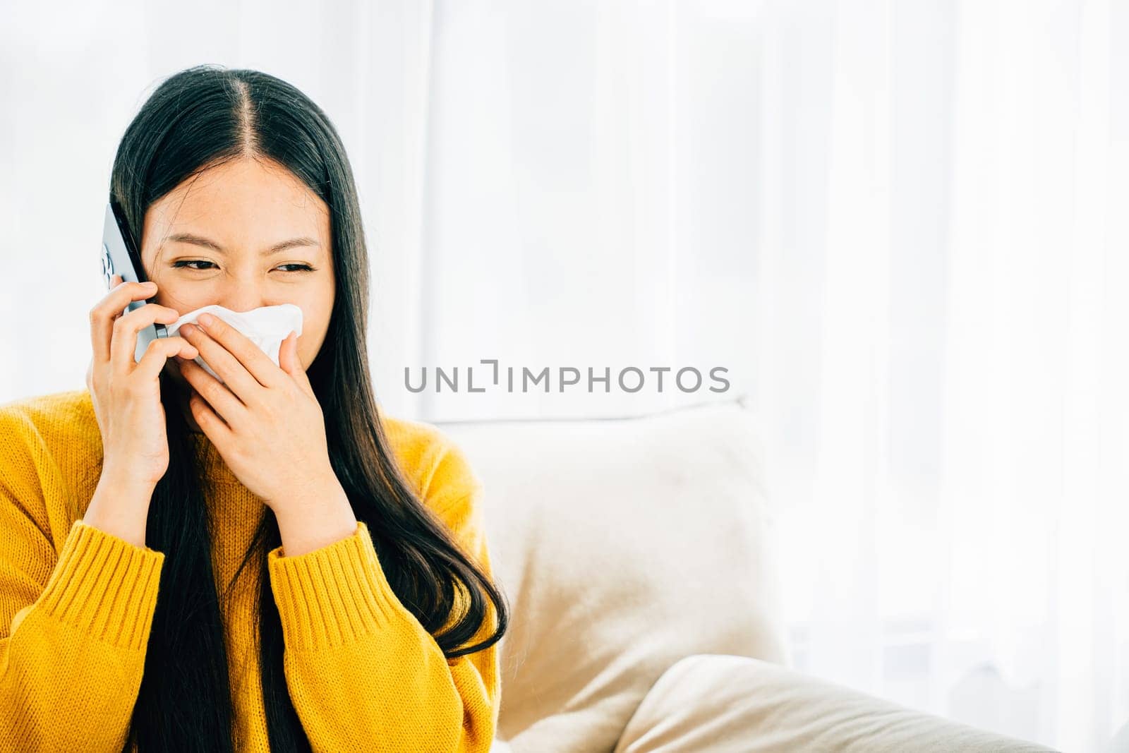 A sick woman calls doctor while blowing wiping nose sneezing on sofa by Sorapop