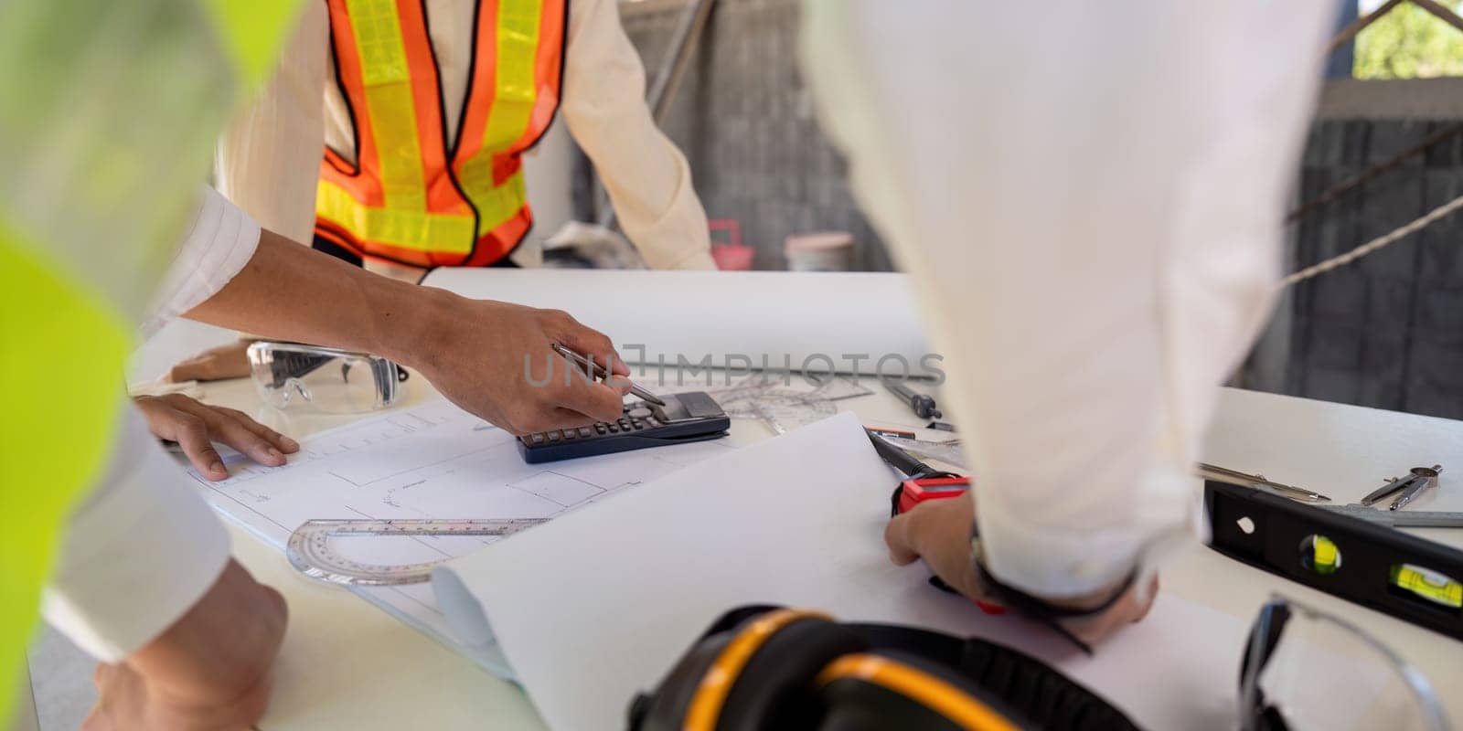 Engineer working on blueprint at construction site, detail of hands and tools. colleagues discussion concept.