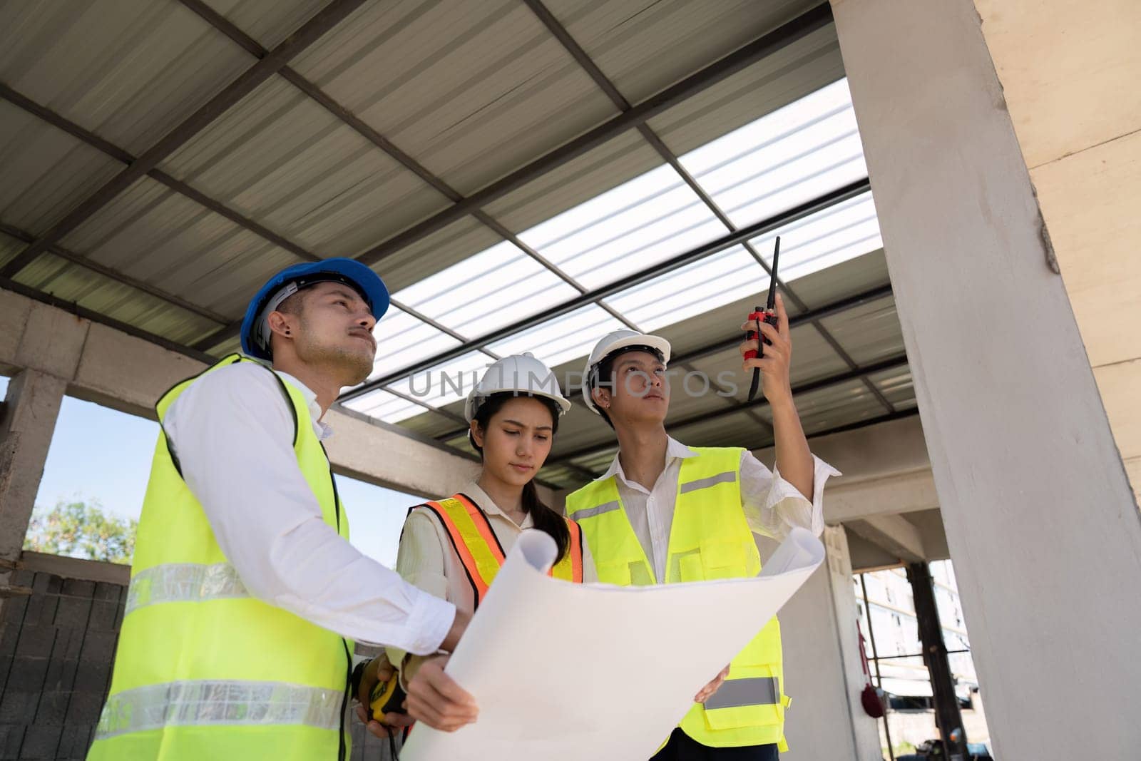 Asian female engineer with colleagues reviewing blueprints at construction site, teamwork concept.