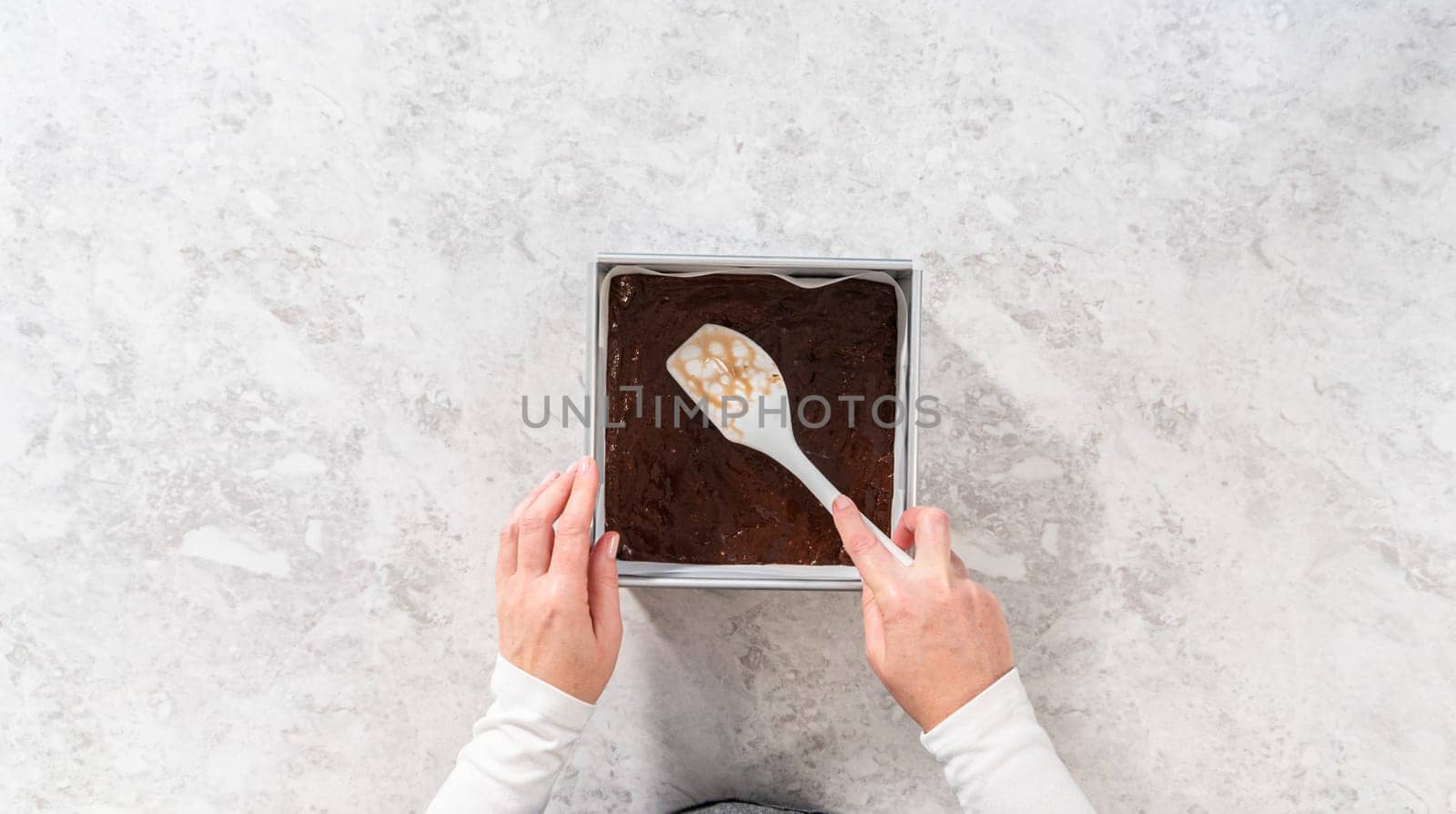 Flat lay. Filling square cheesecake pan lined with parchment paper with fudge mixture to prepare candy cane fudge.