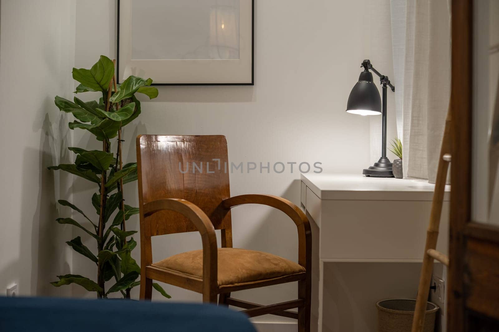 A cozy minimalist home office featuring a wooden chair, desk lamp, houseplant, and white desk, creating a tranquil workspace environment.