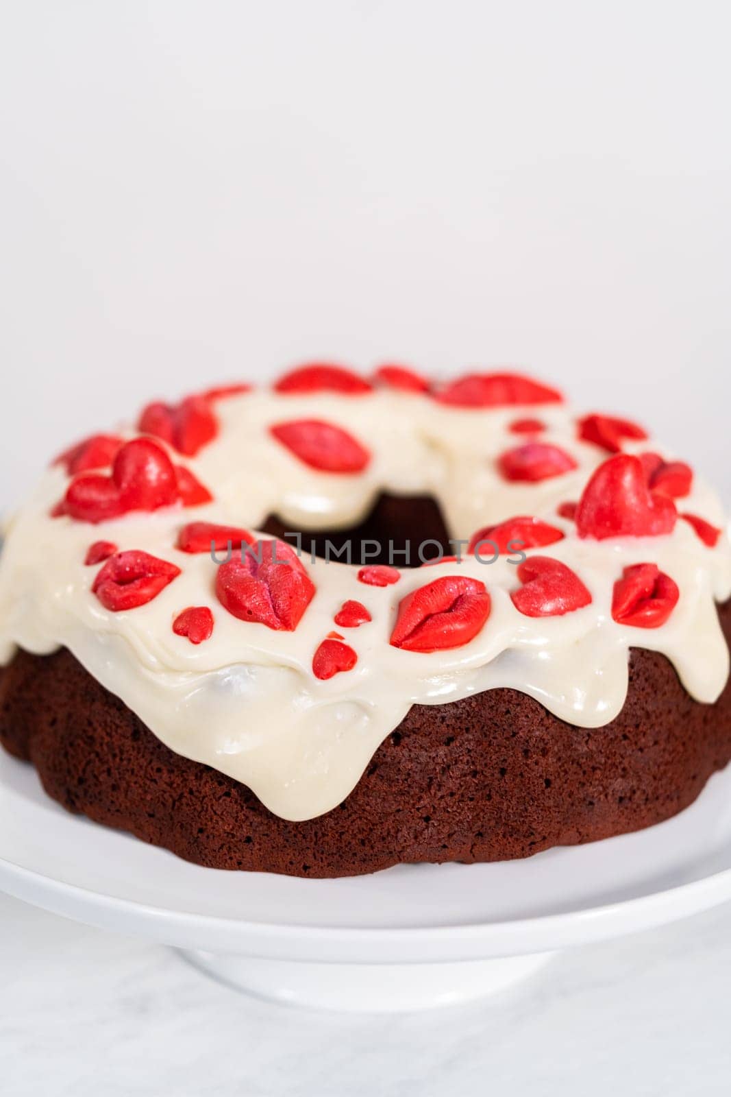 Freshly baked red velvet bundt cake with chocolate lips and hearts over cream cheese glaze for Valentine's Day.