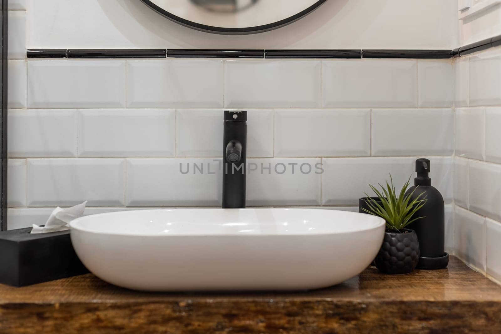 Elegantly designed modern bathroom sink with a black faucet, white tiles, and stylish decor elements, emphasizing minimalism and simplicity.