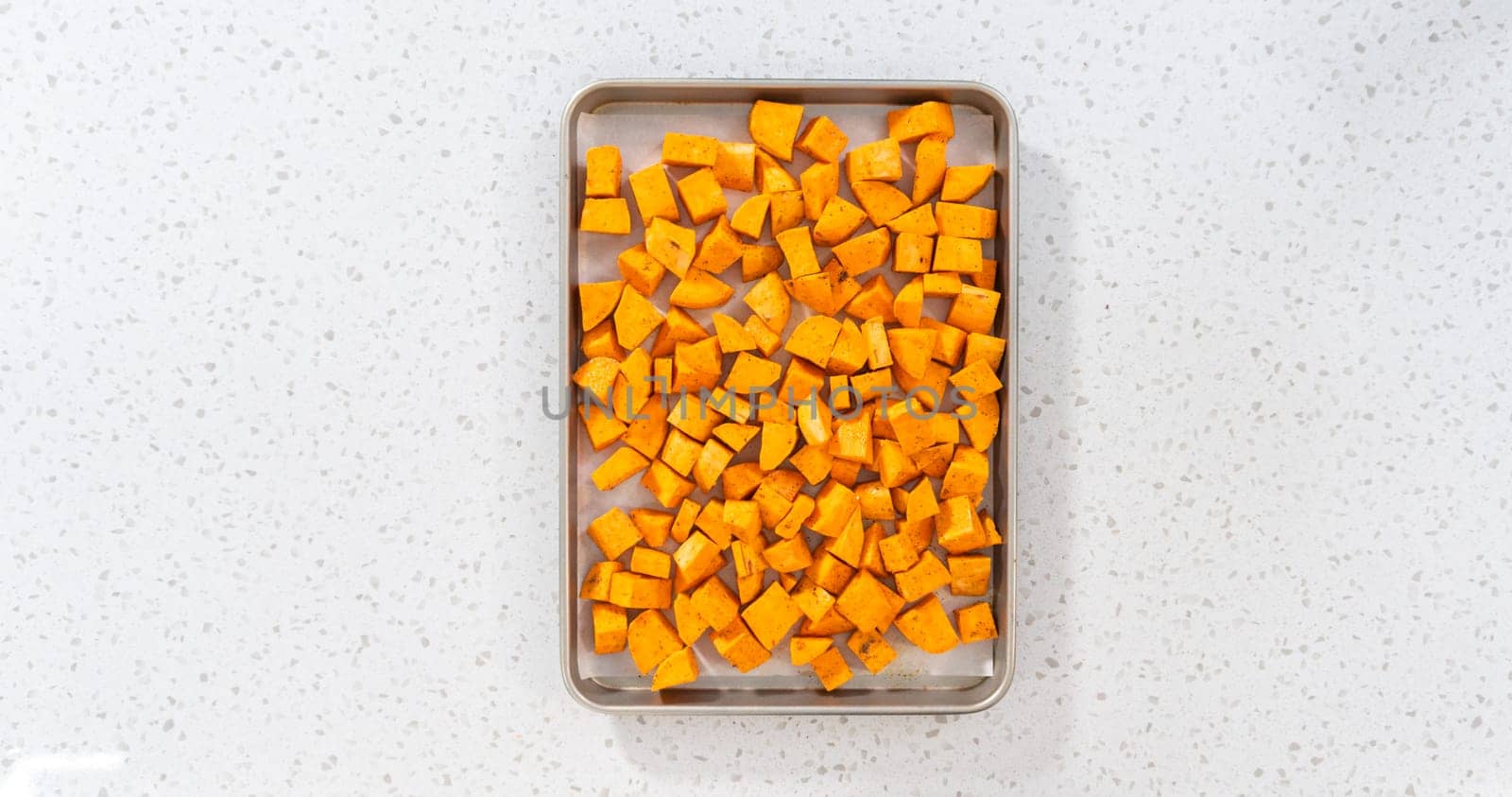 Flat lay. Cubed sweet potatoes on a baking sheet lined with parchment paper to make oven-roasted sweet potatoes.