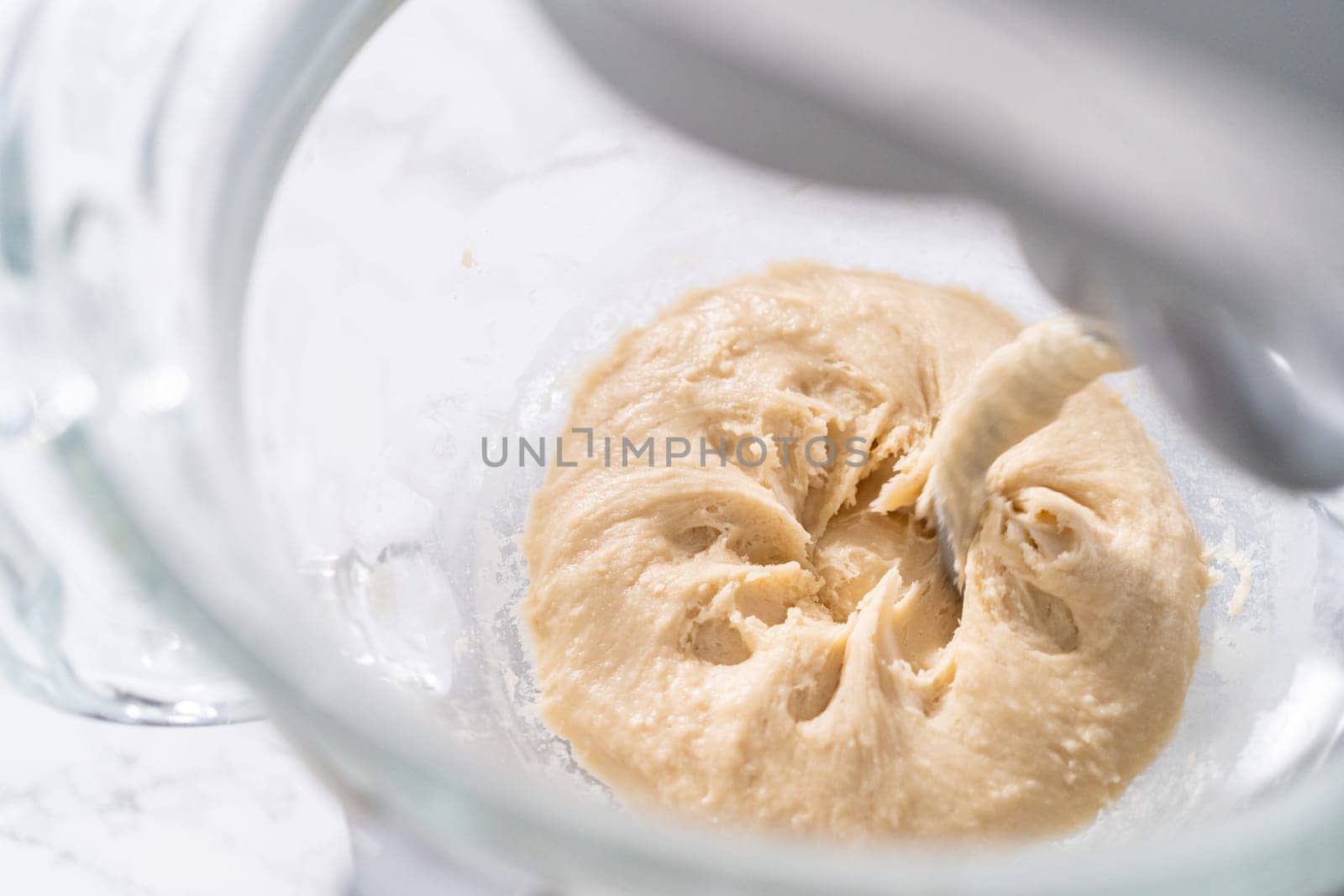 Mixing ingredients in a large glass mixing bowl to pizza dough.