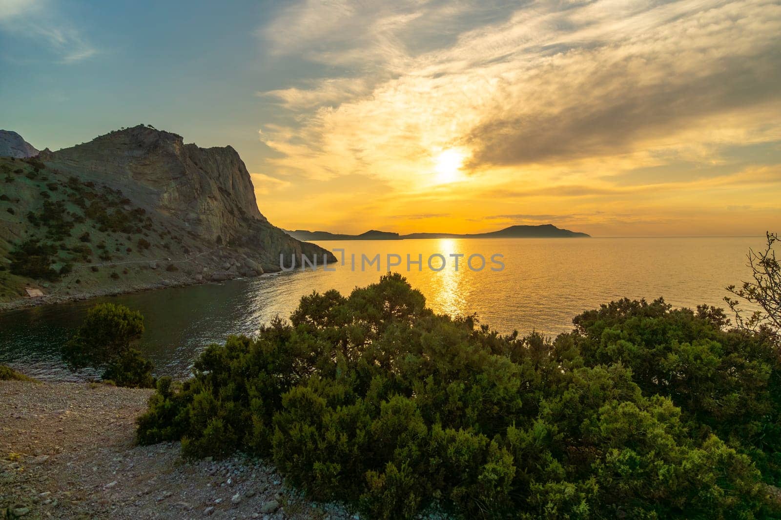 A beautiful sunset over the ocean with a rocky shoreline. The sky is filled with clouds and the sun is setting. by Matiunina