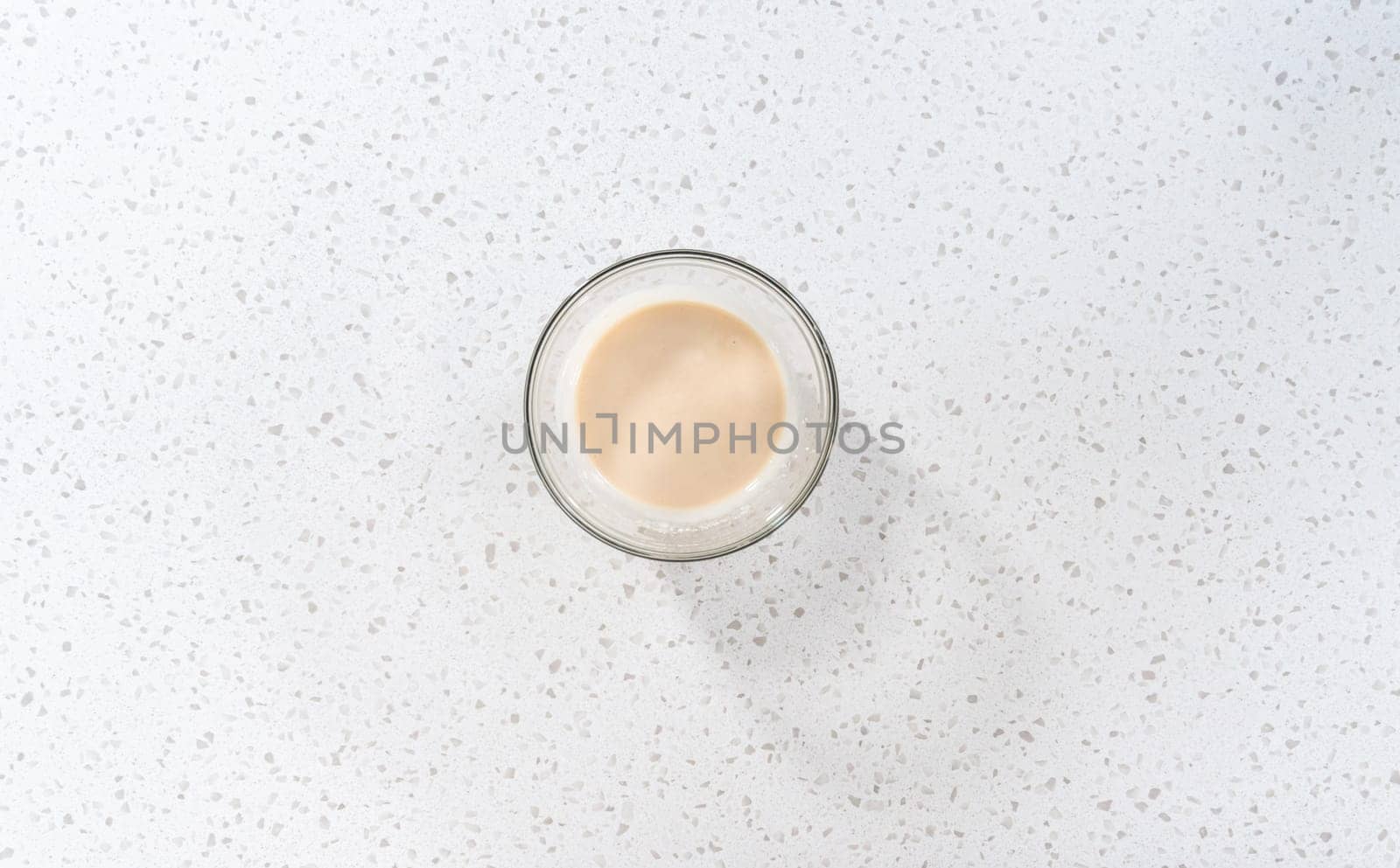 Flat lay. Mixing ingredients with a hand whisk in a glass mixing bowl to make the vanilla glaze.