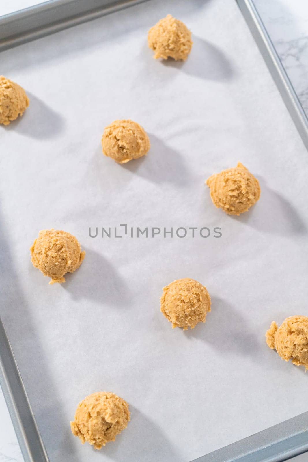 Scooping cookie dough with dough scoop into a baking sheet lined with parchment paper to bake eggnog cookies with a chocolate gingerbread man.