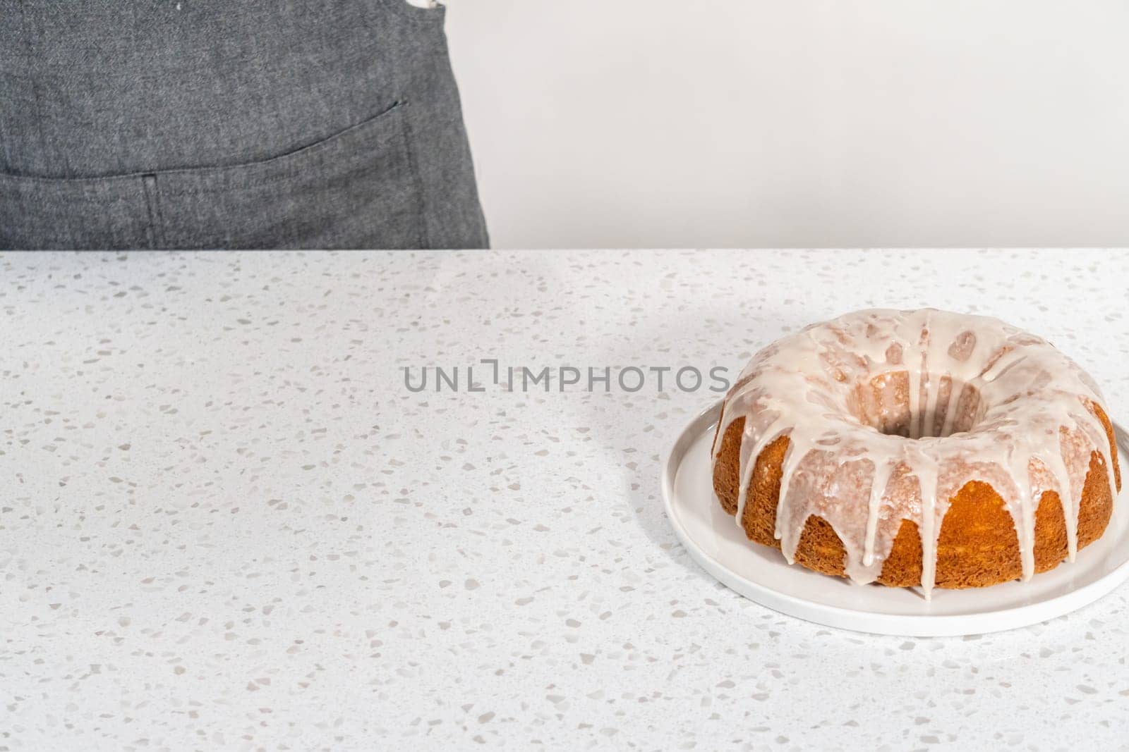 Freshly baked simple vanilla bundt cake with a white glaze on a serving plate.