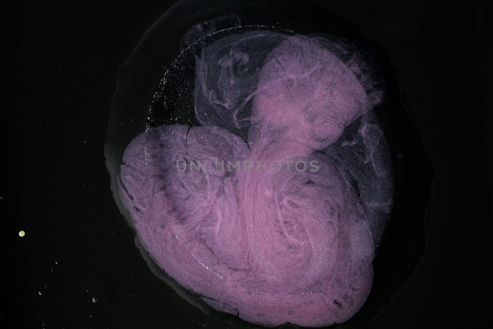 Vibrant blue and pink oil gracefully swirls against a stark black background, showcasing its unique colors and movement.