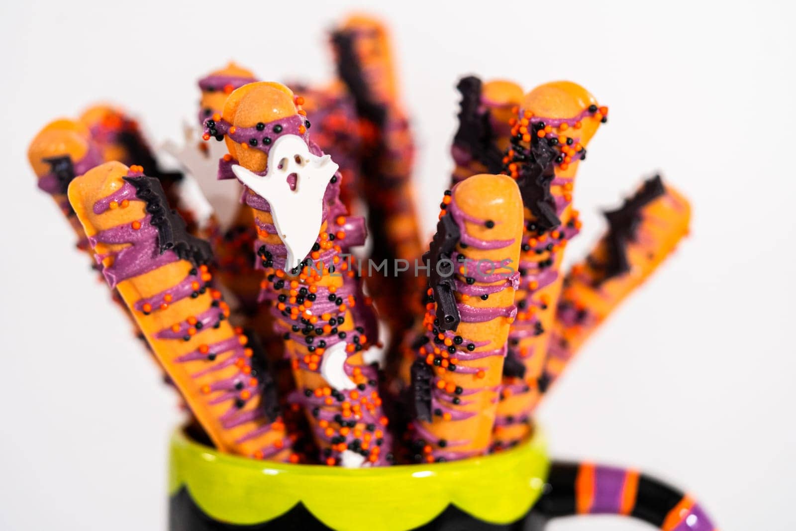 Halloween chocolate-covered pretzel rods with sprinkles in a cup.
