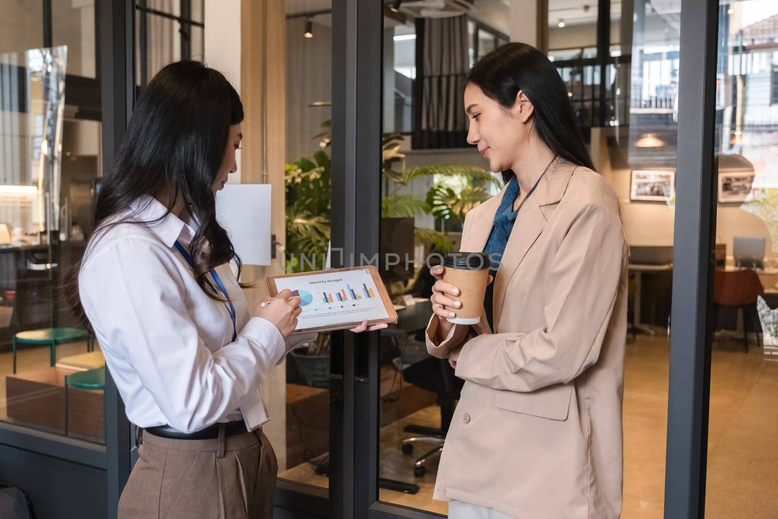 Two young Asian businesswomen discussing financial report on tablet during coffee break.