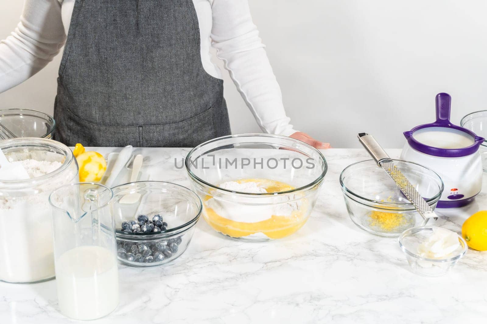 Integrating ingredients in a glass bowl, adeptly stirring with a whisk to craft a tantalizing lemon-blueberry bundt cake.