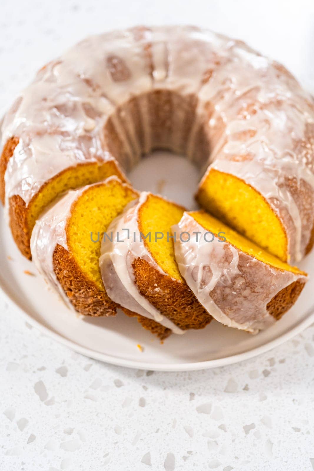 Sliced vanilla bundt cake with a white glaze on a white plate.