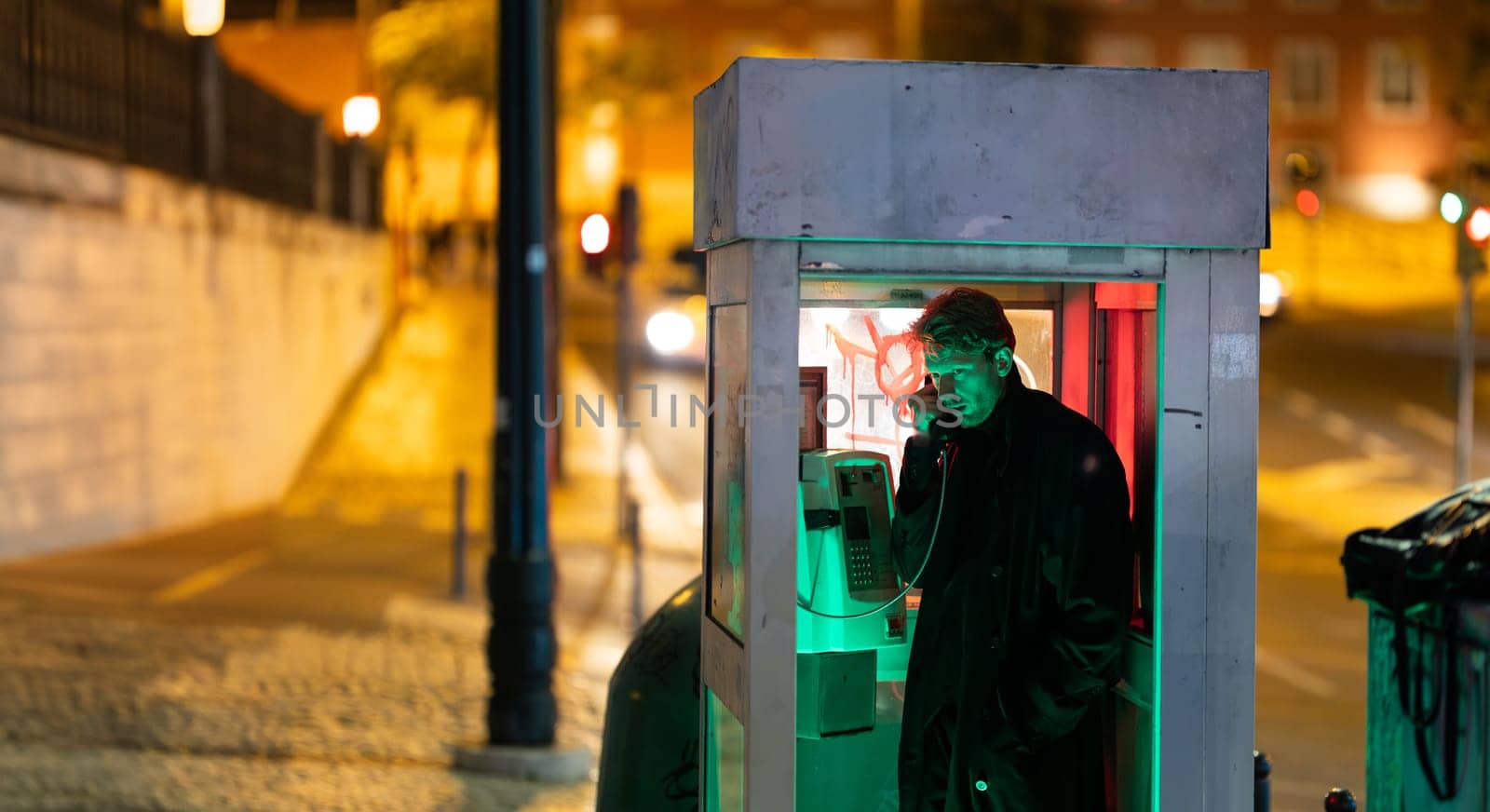 A man is talking on a phone at noir style in booth The image has a dark and moody atmosphere, with the man's face illuminated by the phone's light
