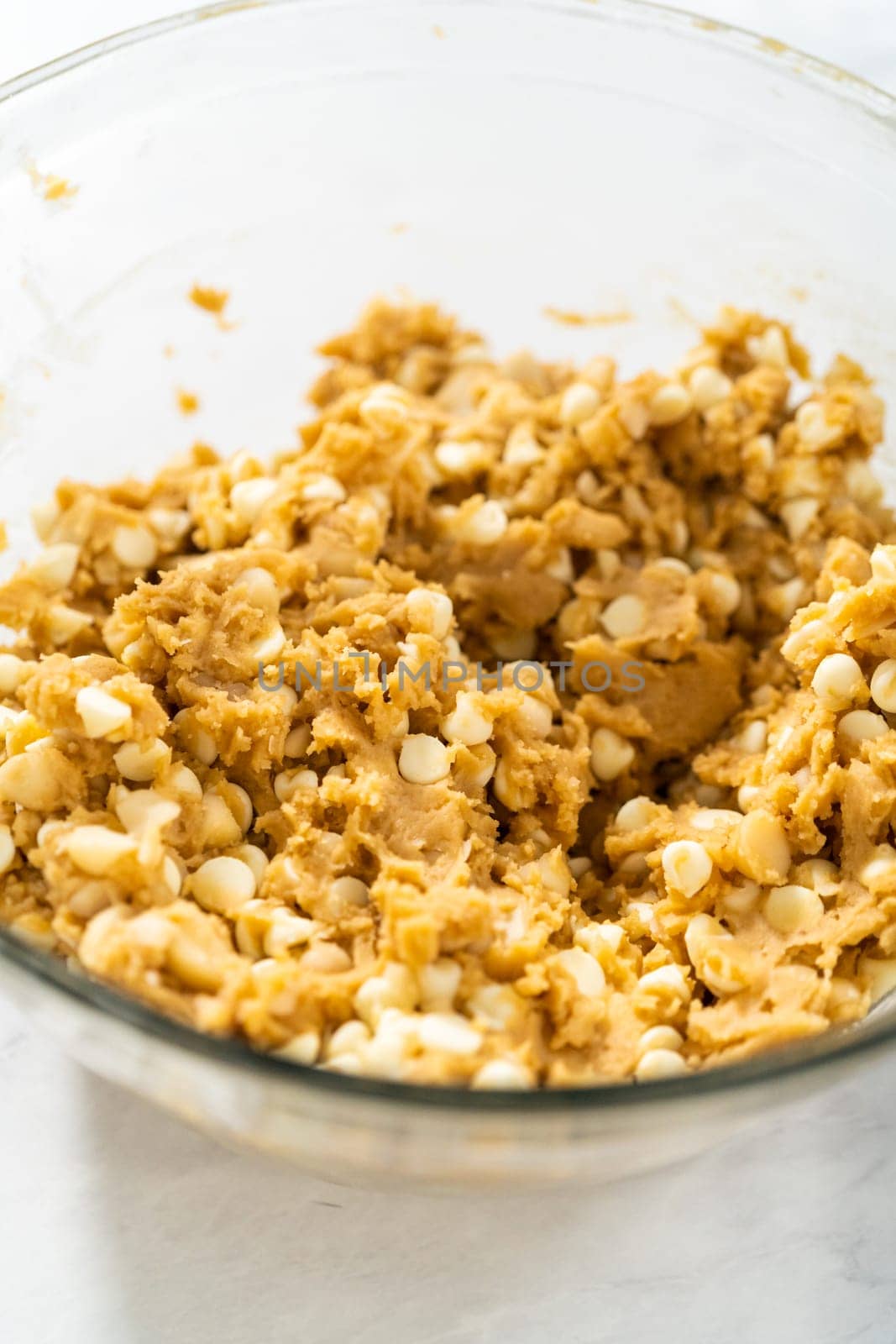 Mixing wet and dry ingredients with a hand whisk in a glass mixing bowl to bake white chocolate macadamia nut.