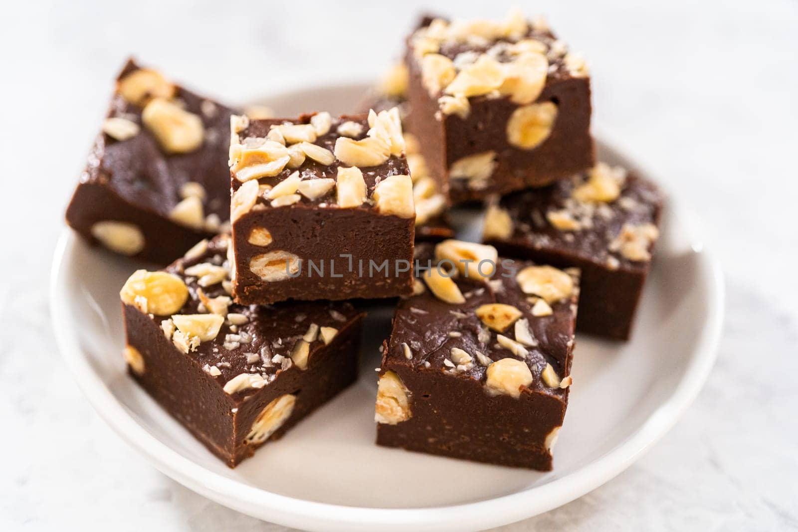 Homemade chocolate hazelnut fudge square pieces on a white plate.