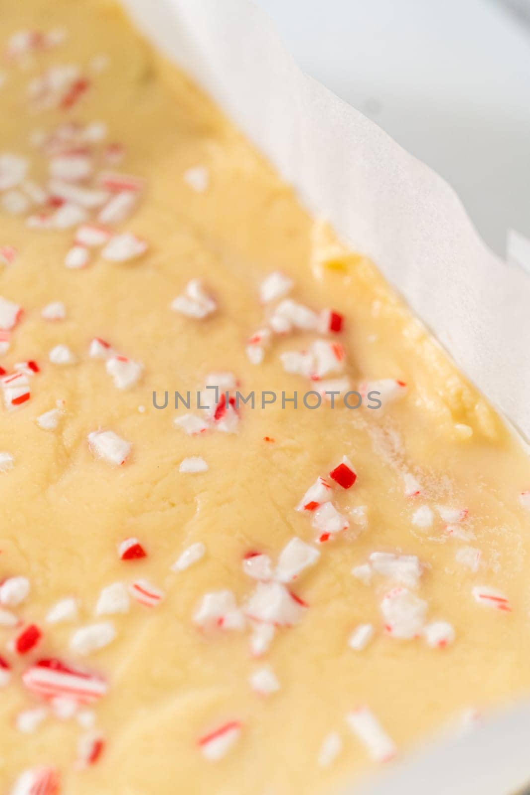 Removing candy cane fudge from a square cheesecake pan lined with parchment.