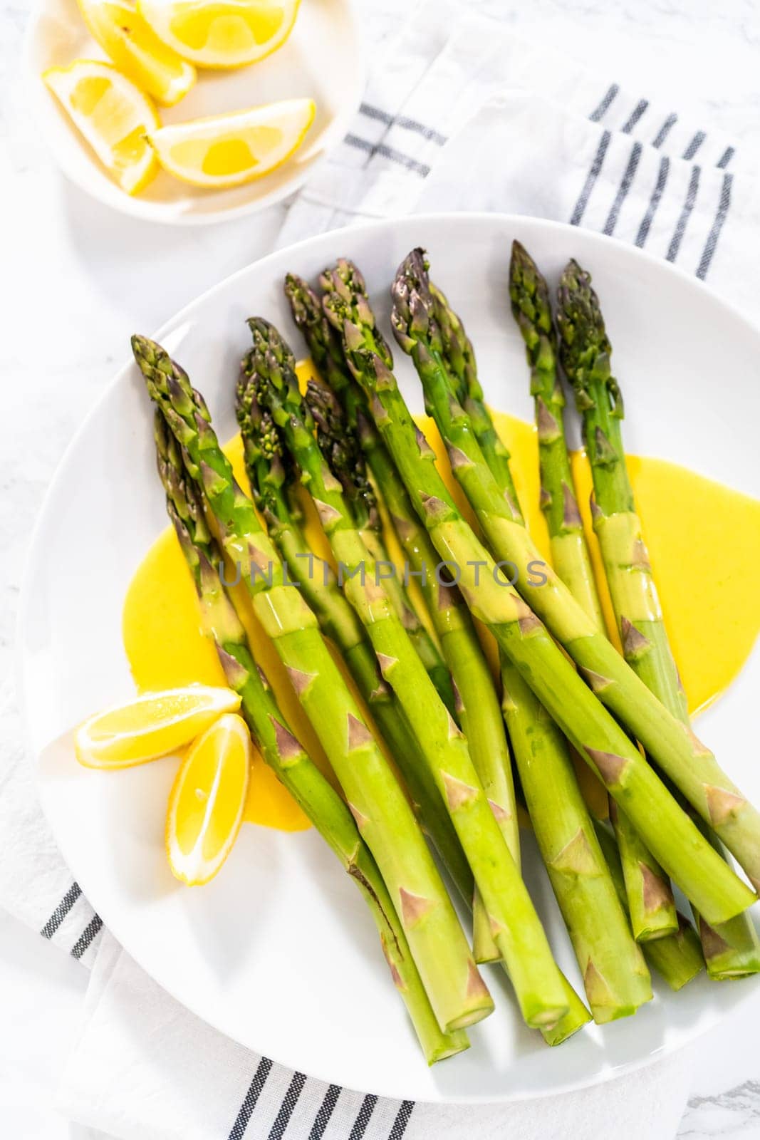 Serving steamed asparagus with homemade hollandaise sauce with lemon wedges on a white plate.