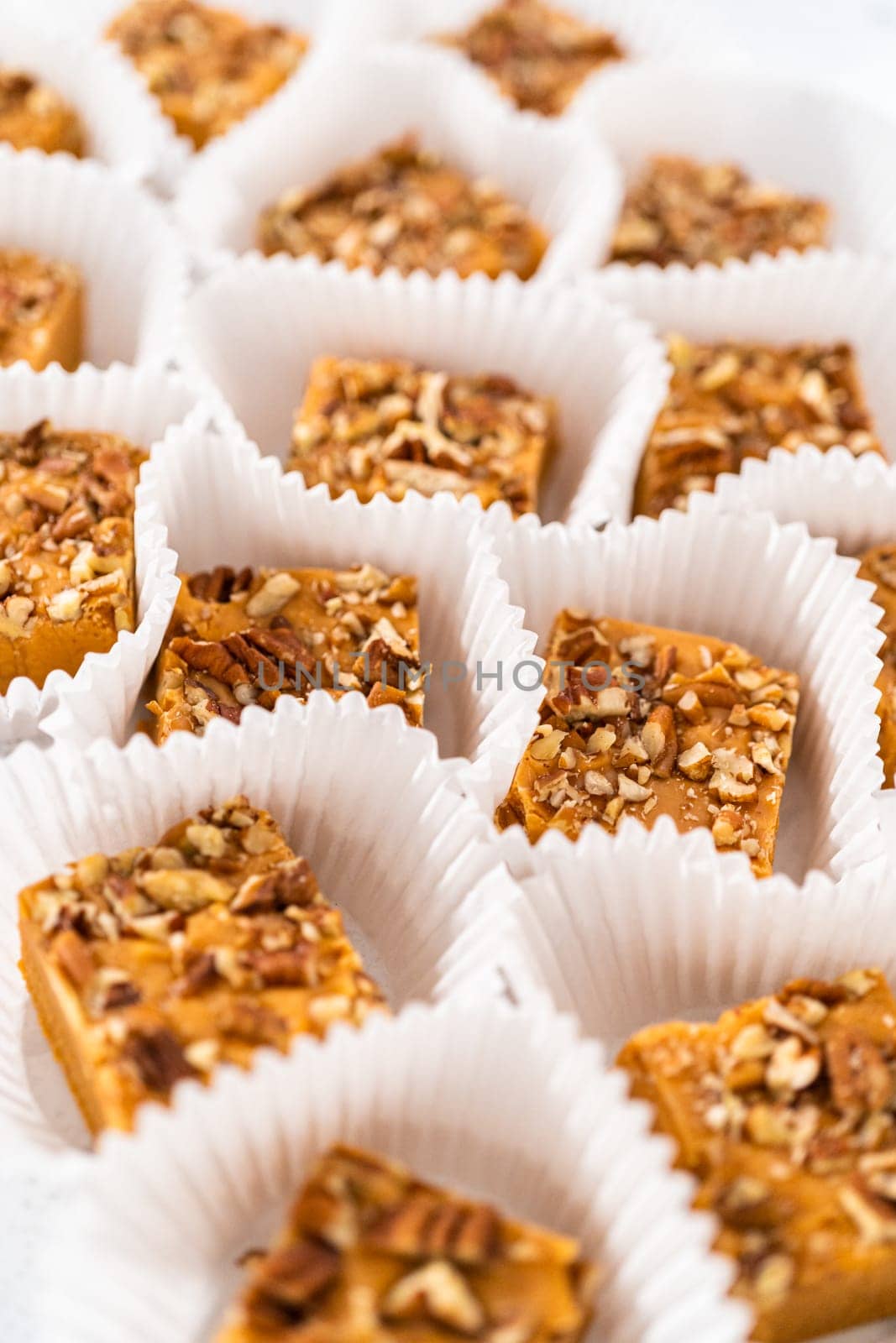 Homemade pumpkin spice fudge square pieces in white paper cupcake liners on a kitchen counter.