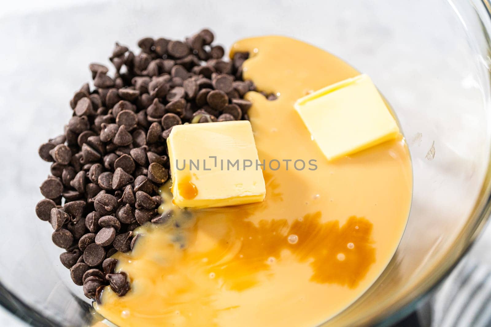 Melting chocolate chips and other ingredients in a glass mixing bowl over boiling water to prepare chocolate hazelnut fudge.