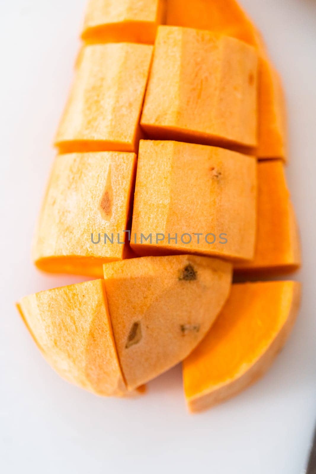 Cutting sweet potatoes into cubes on a white cutting board to make oven-roasted sweet potatoes.